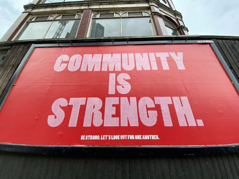 Auf dem Bild ist ein rotes Plakat zu sehen. Darauf steht groß "Community is strength"